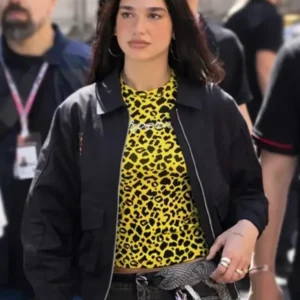 Dua Lipa wearing a stylish Porsche jacket at the F1 Grand Prix Monaco, featuring a sleek racing design with logo detailing and a modern sporty fit.