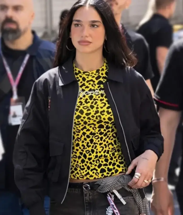 Dua Lipa wearing a stylish Porsche jacket at the F1 Grand Prix Monaco, featuring a sleek racing design with logo detailing and a modern sporty fit.