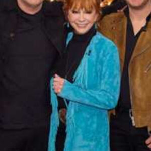 Reba McEntire wearing a blue suede fringe coat on The Voice Season 28, featuring long fringes and Western-inspired detailing.